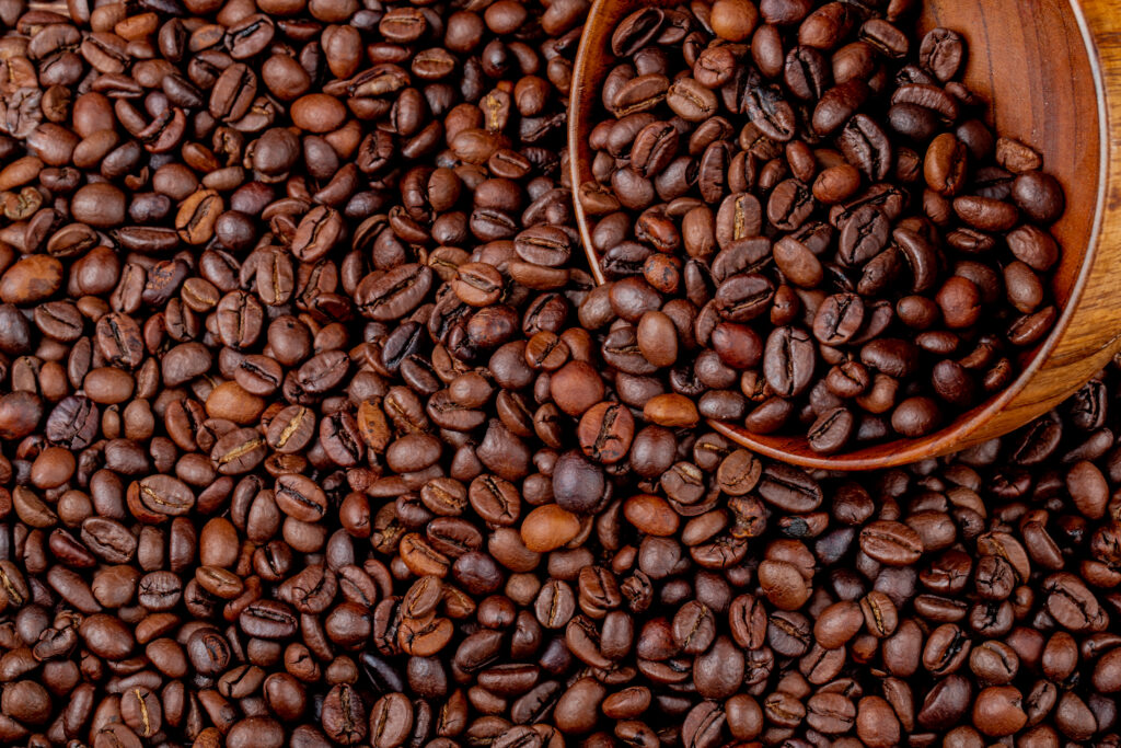 top view of roasted coffee beans scattered from wooden bowl on coffee beans background